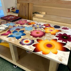 Spray-painted wooden flowers laid out on a work bench in the workshop.