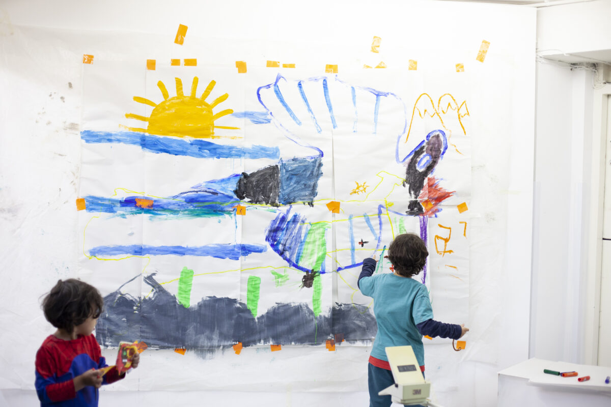 Two children working on a large collaborative wall painting including a sun and bird.