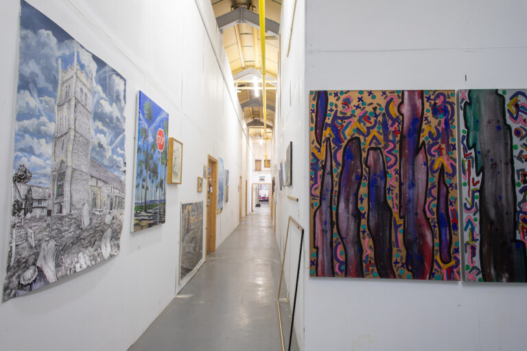 Photograph of a long corridor into artists studios, artwork hung on the walls during Essex Open Studios