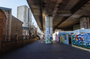 Photograph of colourful activity in a single-storey building under an urban flyover.