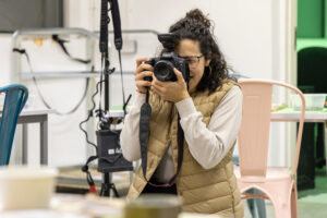 Photograph of Andreia Sofia taking a photograph in a bright space, indoors.