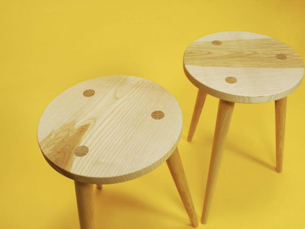 Two three-legged stools against a canary yellow background.