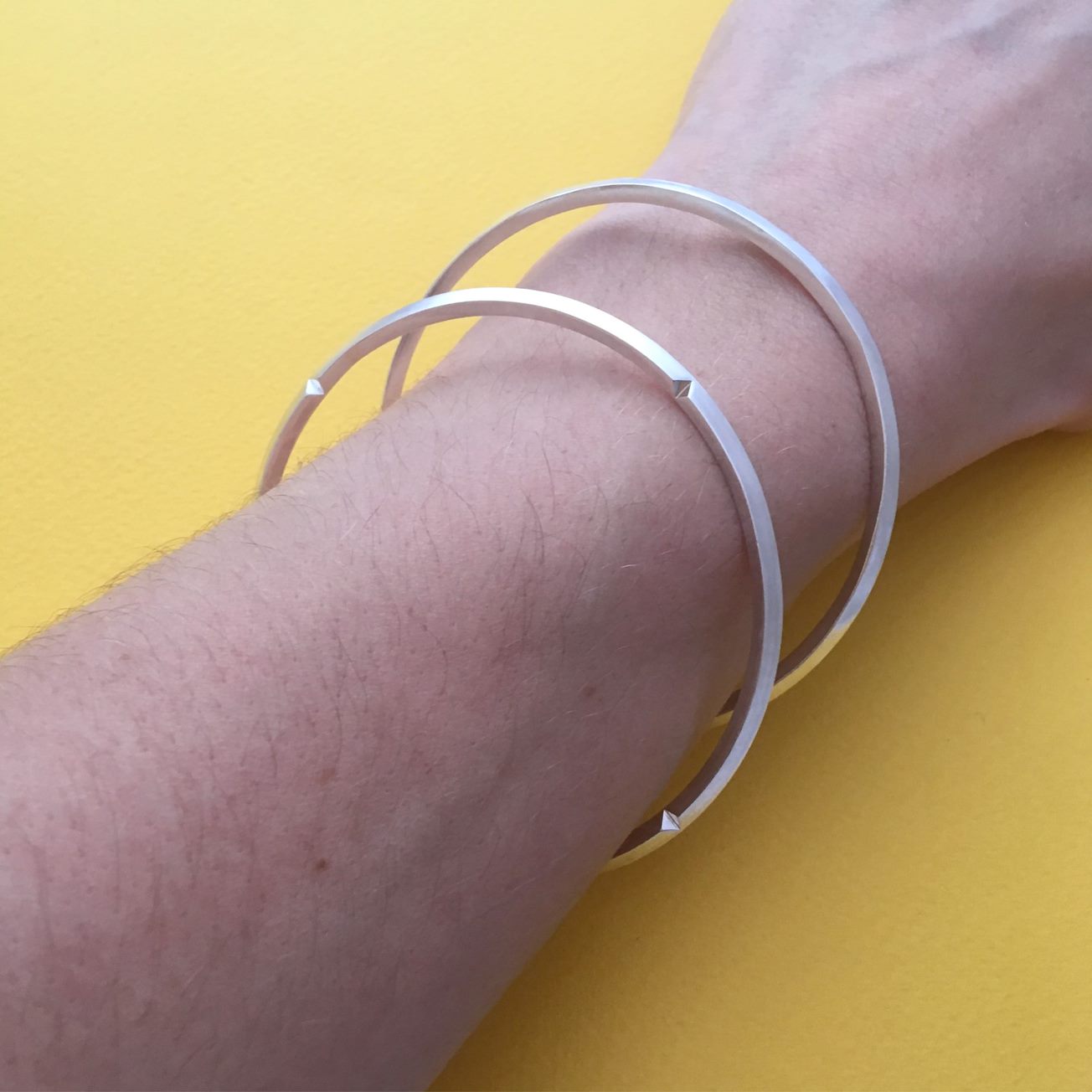 Detail of a wrist with two silver bangles, against a yellow background.