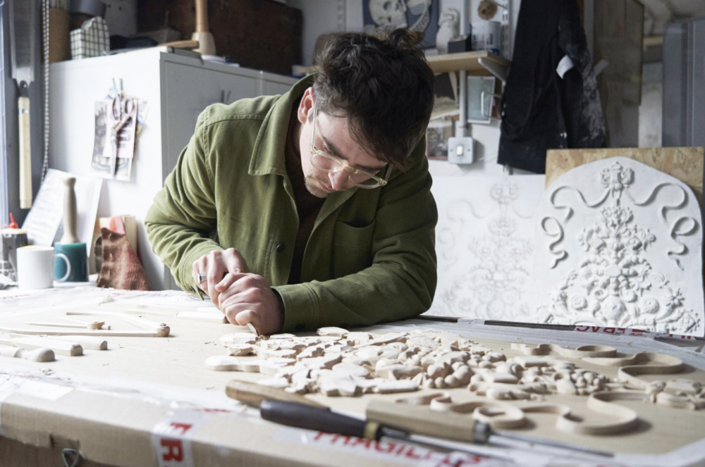 Person wood carving on a large table, in a studio, indoors