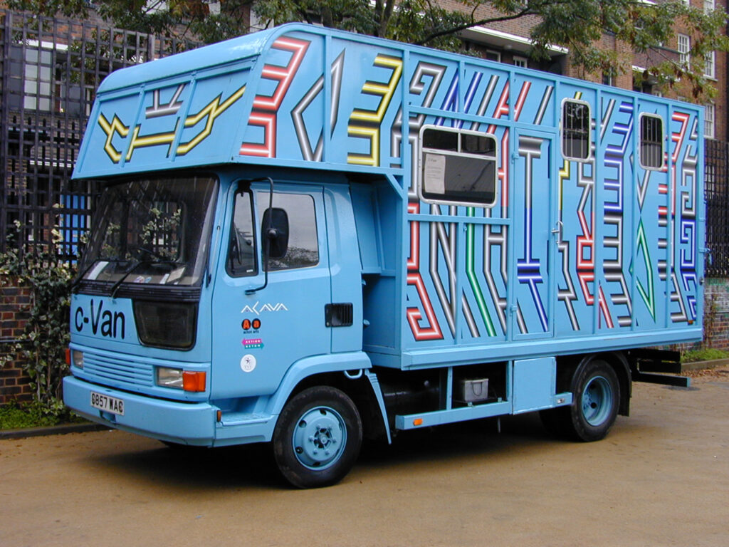 Photograph of a blue converted horse box with painted/sprayed/vynil artwork by international artist Mark Titchner, outdoors