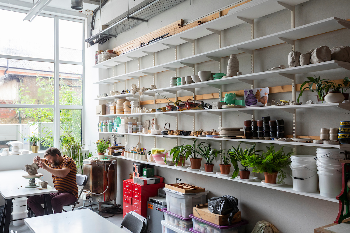 Photograph of a ceramicist working on a table in a large and modern ceramics studio, a large window at the back