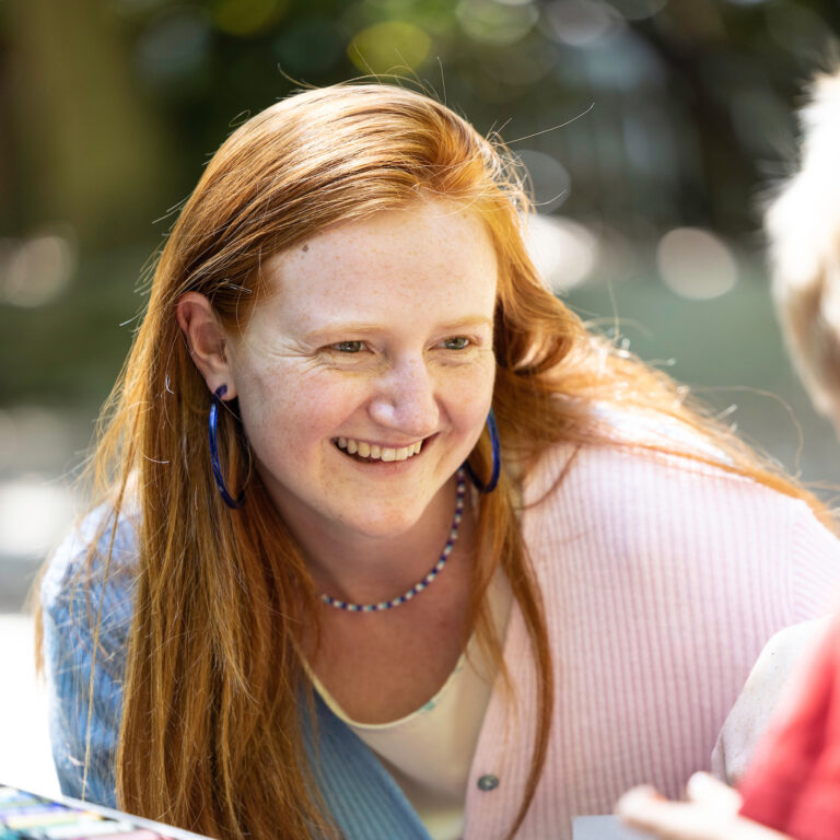 Close-up of Mattie smiling at a child, outdoors in a bright green space