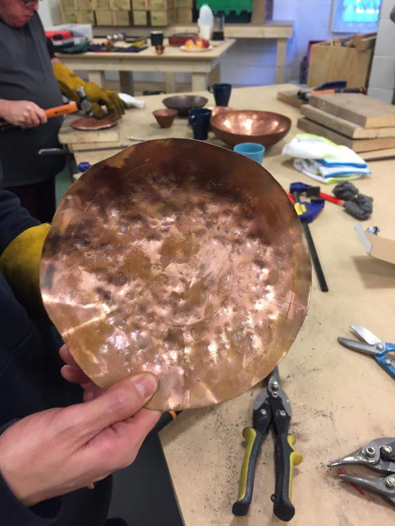 Close up of a hand holding a circle of copper being modelled, in a makerspace, indoors