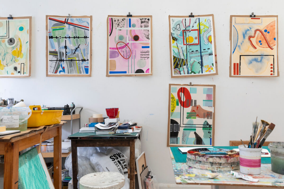 Artist's studio with colourful abstract watercolours on the wall, art materials in sue on small tables