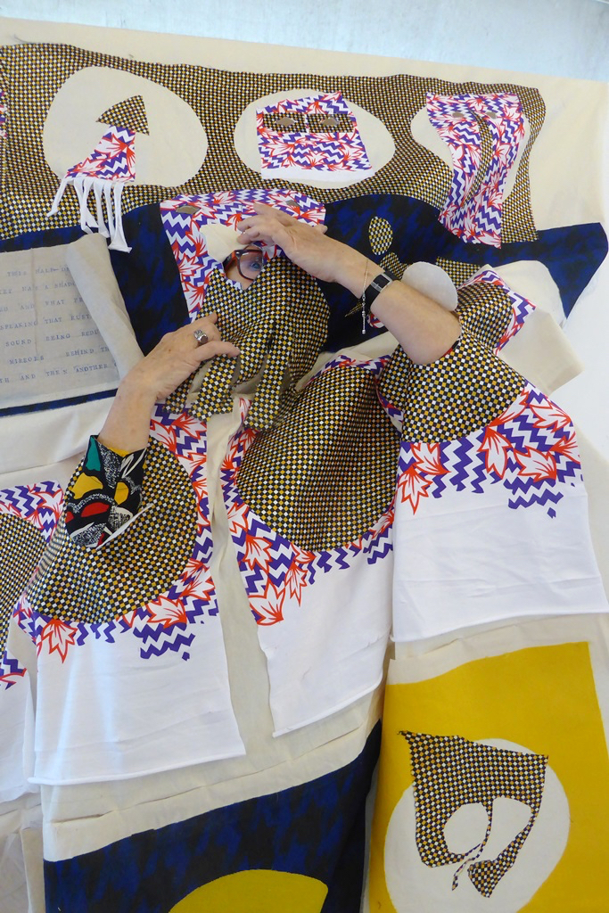 Portrait of ACAVA artist Marisa Rueda looking through a hole in a handmade textile piece.