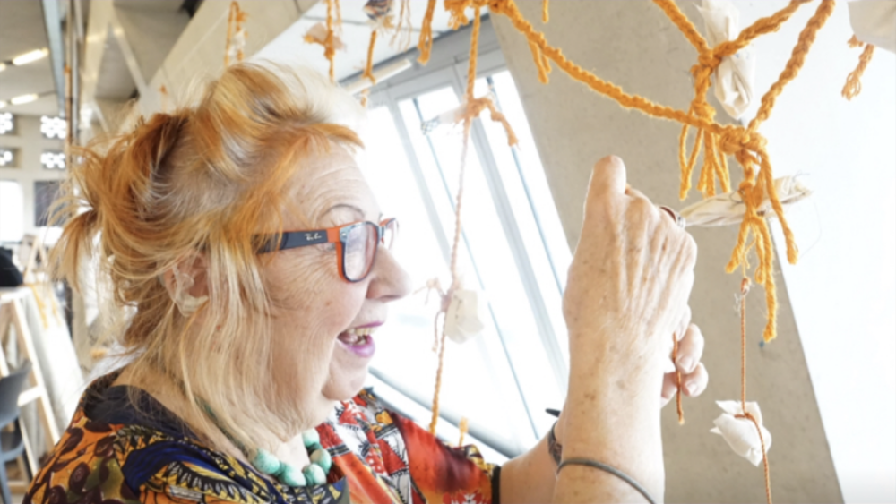 Profile photograph of artist Marisa Rueda smiling while working on a string sculpture in a bright space, indoors.