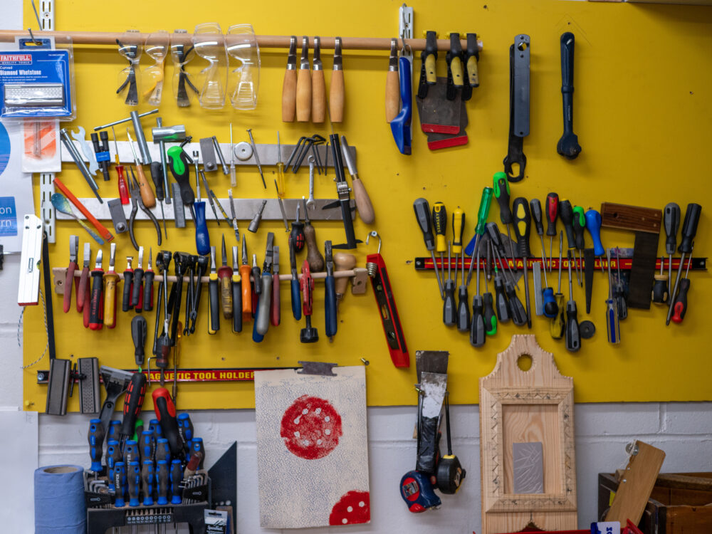 Various carving and other small carpentry tools fixed to a yellow wall in a community makerspace, indoors.