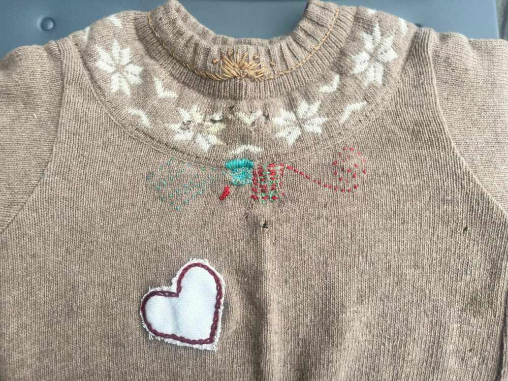 Photograph of a woollen jumper mended with handmade patches and colourful stitches.