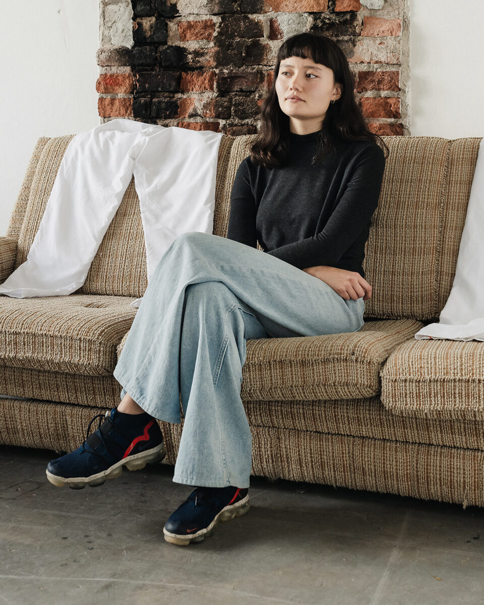 Photograph of Amelia Tan sitting with crossed legs on a light brown sofa.