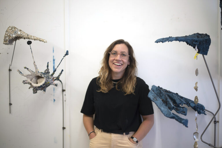 Portrait of artist Anna Reading smiling and posing next to her artwork