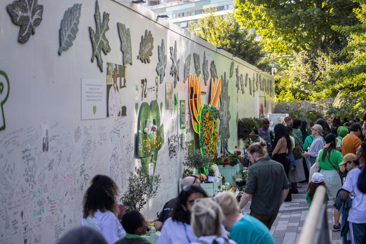 Profile view of the hoarding at the foot of Grenfell Tower with mosaics created during phase one and phase two of the project, with a large number of people paying their respects to the victims.