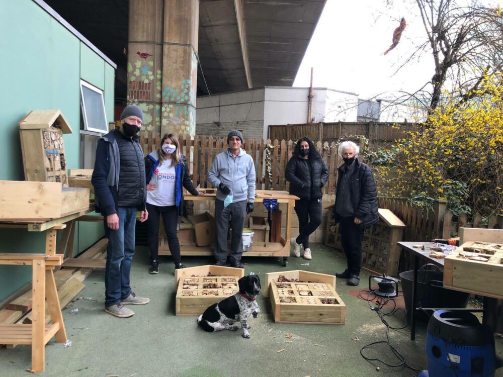 A group o people posing for a photo, relaxed, while making bug hotels in a community makers space, outdoors, in a yard.