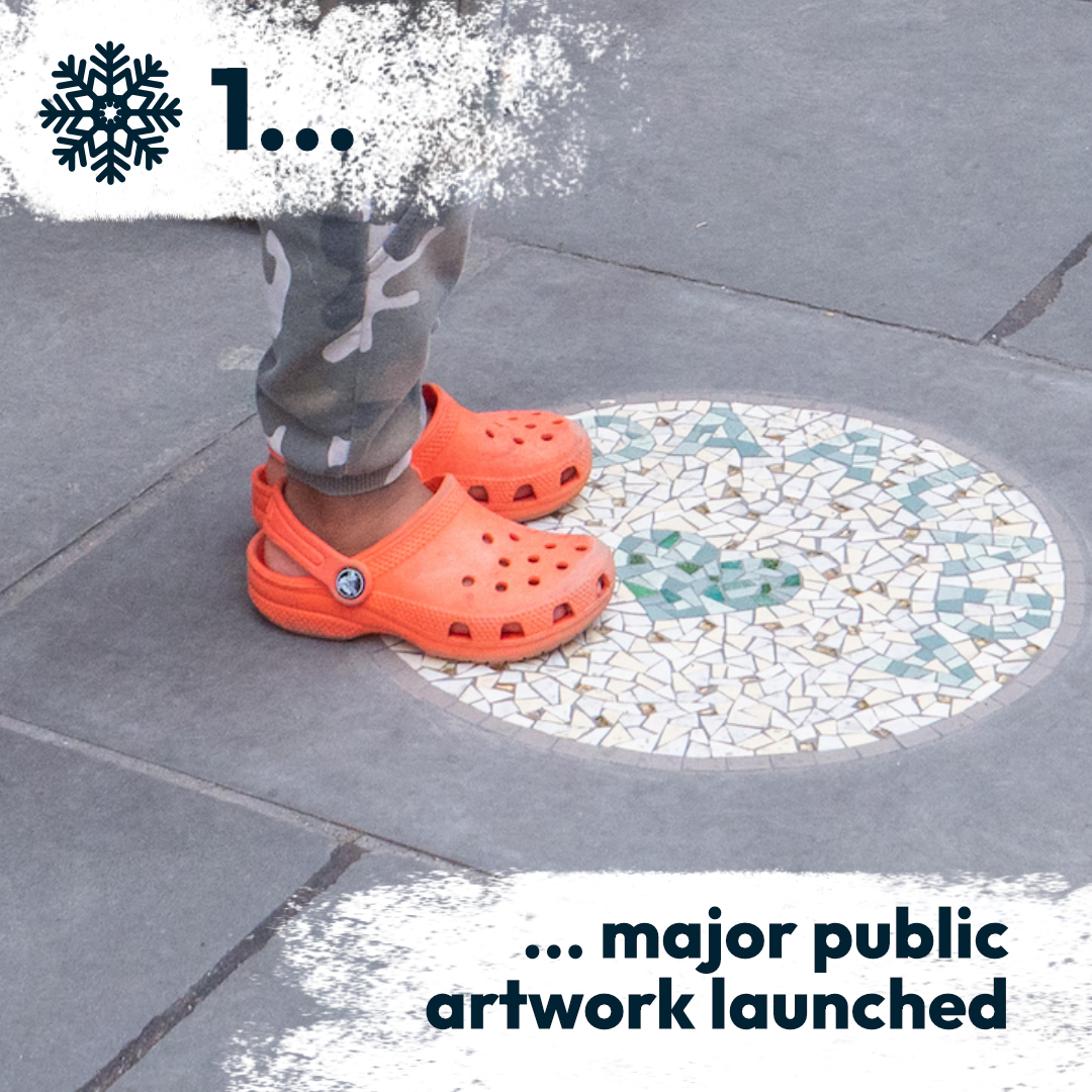 Closeup of a child's feet wearing orange crocs stepping onto a circular mosaic artwork on a stone slab on the street, outdoors.