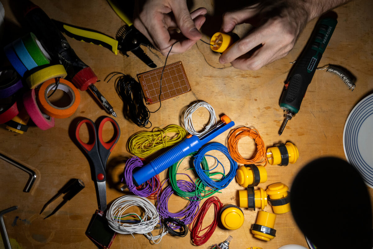Close-up of hands on a table assembling electric wire of different colours, with soldering and wire-cutting tools.