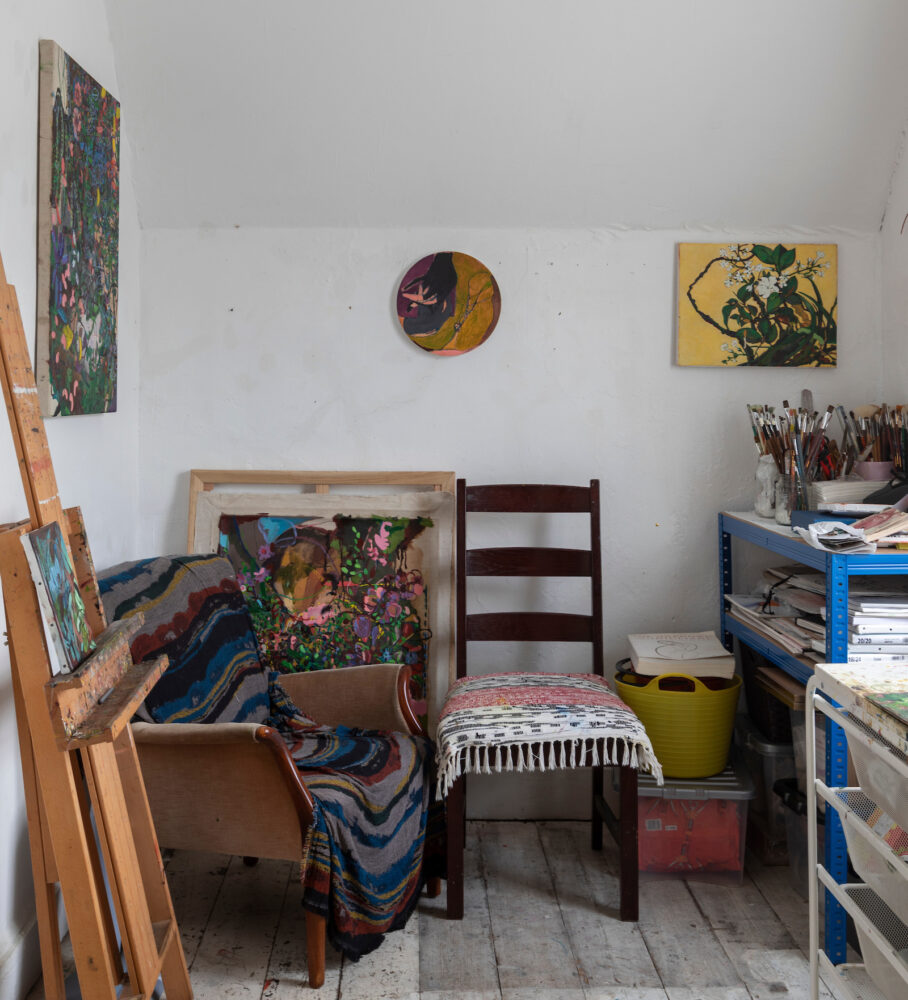 Photograph of a small cosy studio with a chair, lounge chair with rug and paintings hanging on the wall.