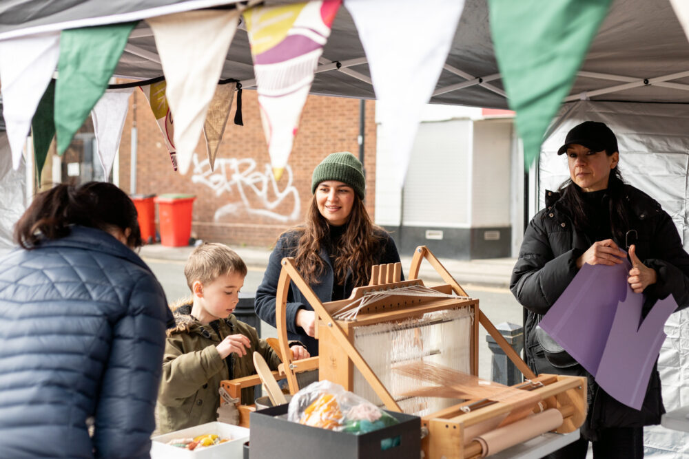 Photograph of a creative activity happening in a stall, outdoors on a sunny day.