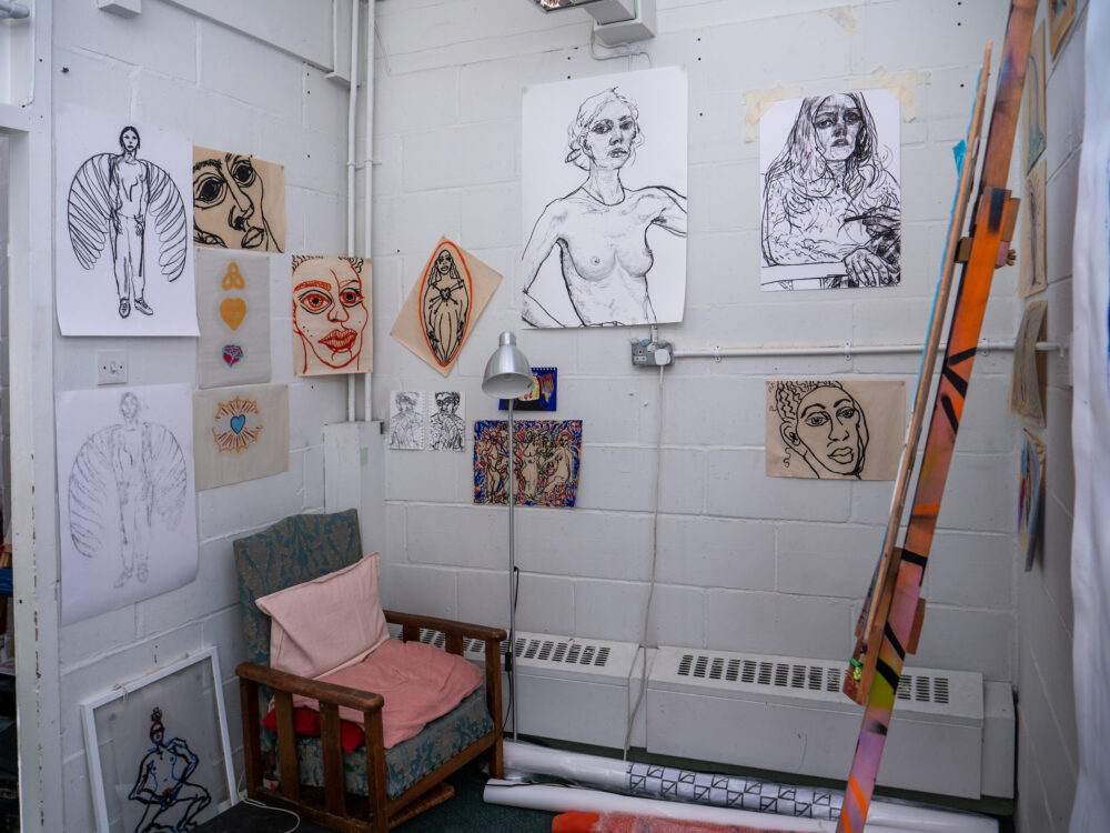 Detail of an artist's studio, figurative sketches on the wall, comfy chair on the corner.