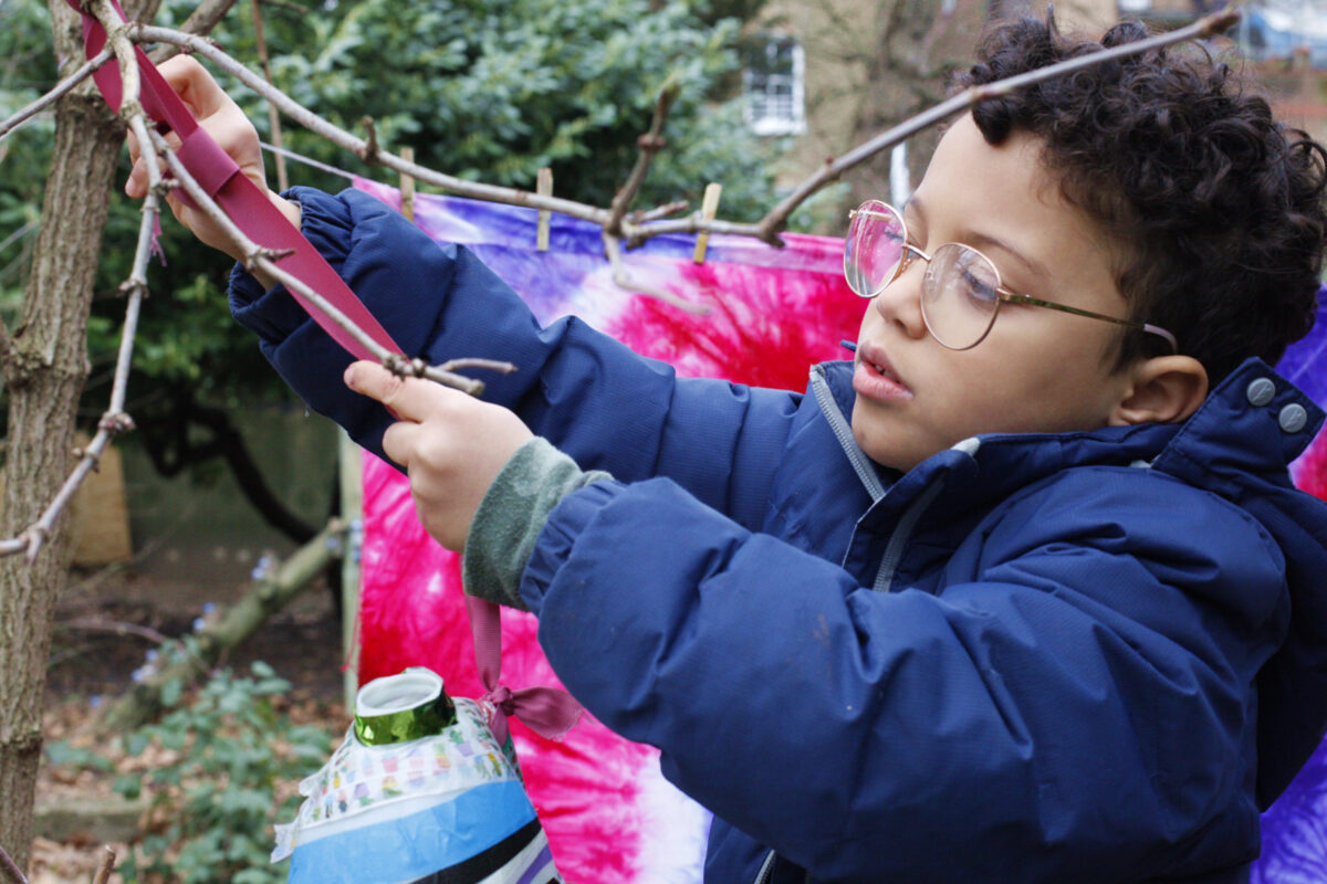 Photograph of a child making a creative object from a ribbon and tree branch.