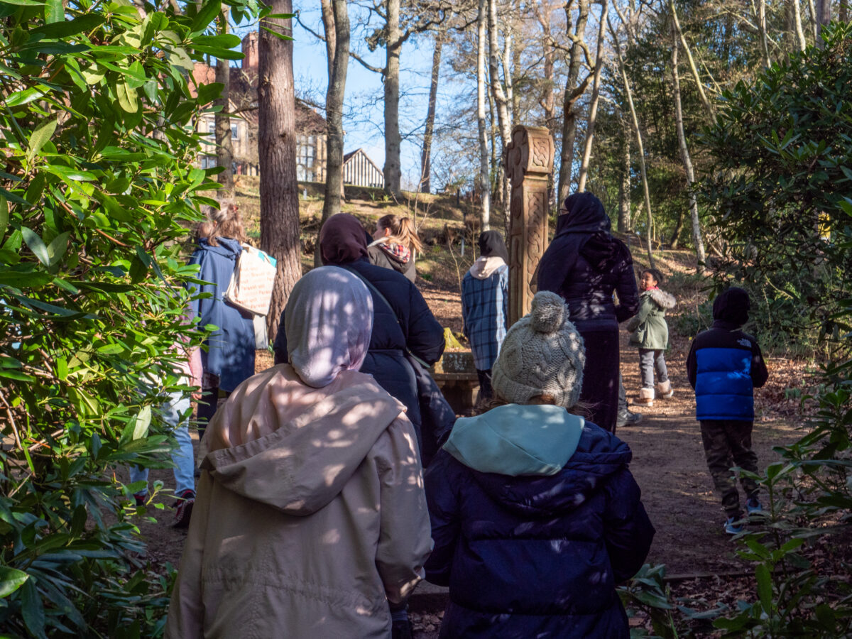 A group of families walking in the woodlands towards a house on top of a hill.