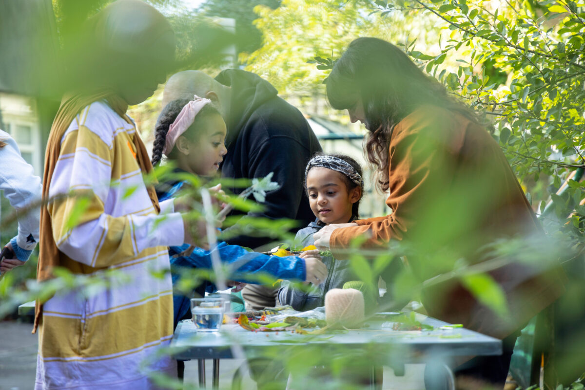 Image of families working creatively around a table, outdoors, in a park.