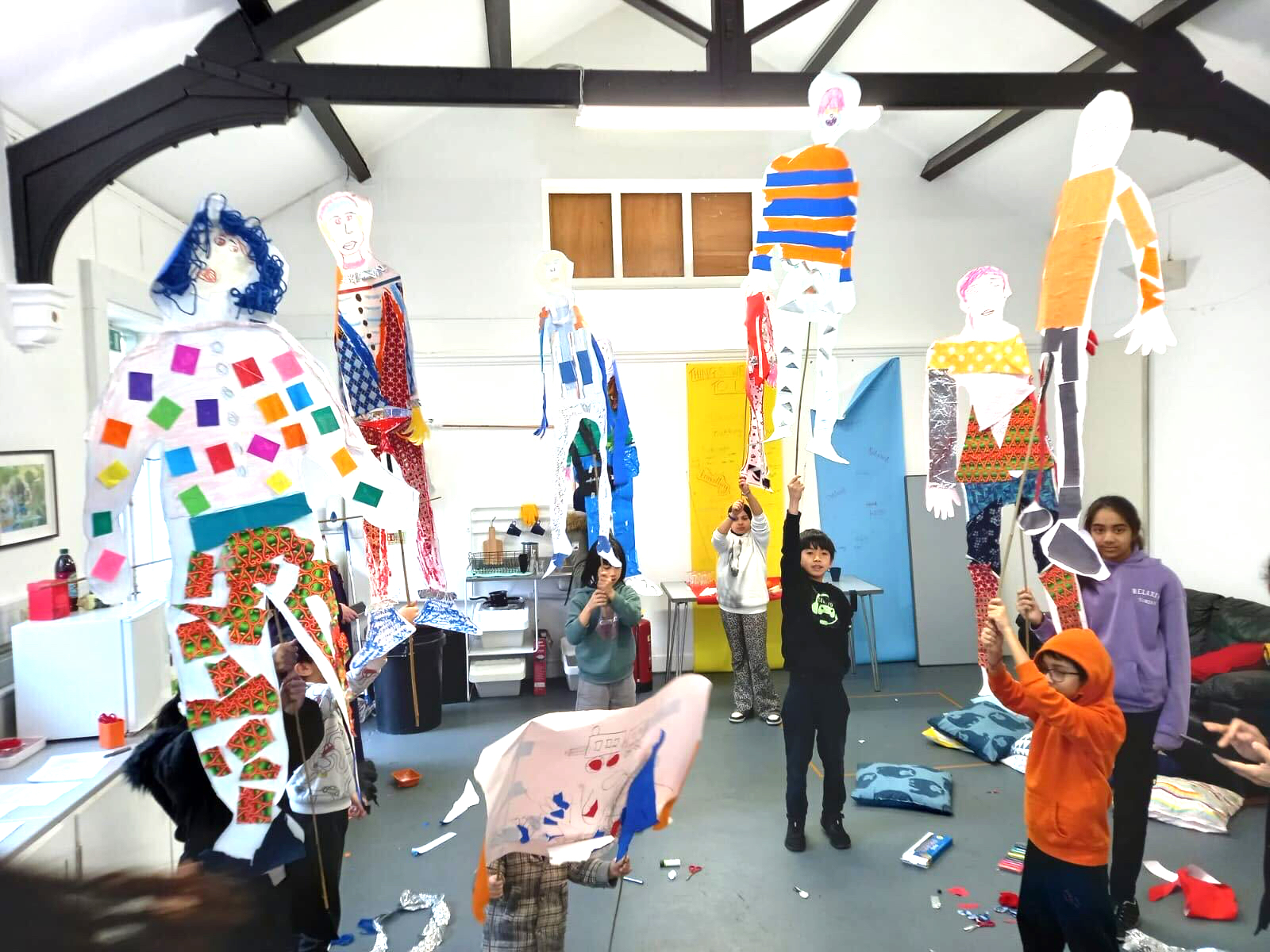 Photograph of a group of children holding their life-size colourful mannequins, during a creative workshop, indoors.