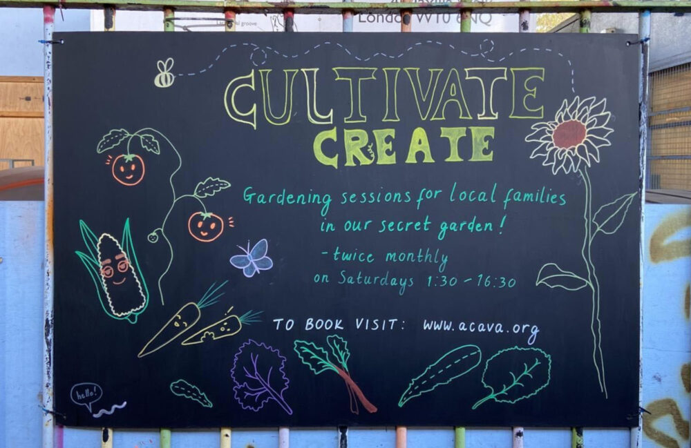 Photo of a blackboard fixed to metal railings depicting handmade drawings of flowers, smiley vegetables, and the text "Cultivate Create / Gardening sessions for local families in our secret garden!".