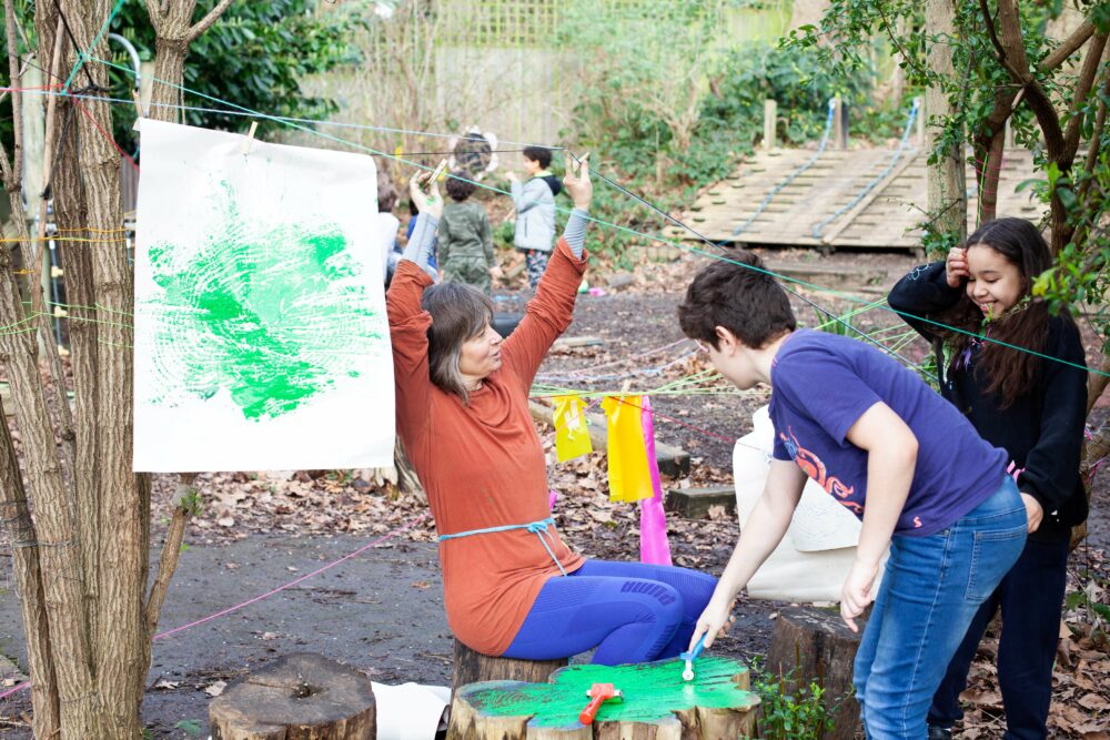 Photograph of an adult and children experimenting with tree stump prints, outdoors in a forest school garden.